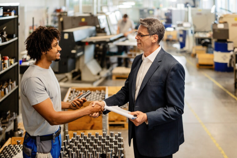 Happy businessman greeting African American steel worker while visiting industrial facility.